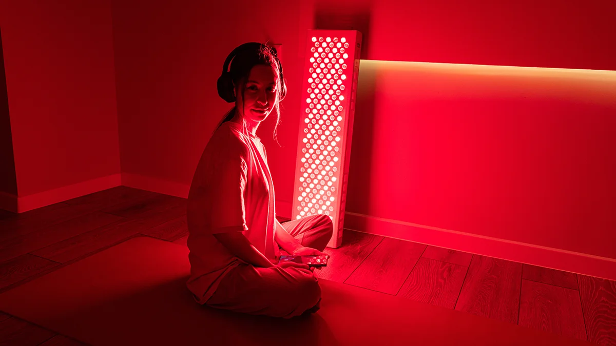 A woman sittting in front of a red light therapy panel in a dark room